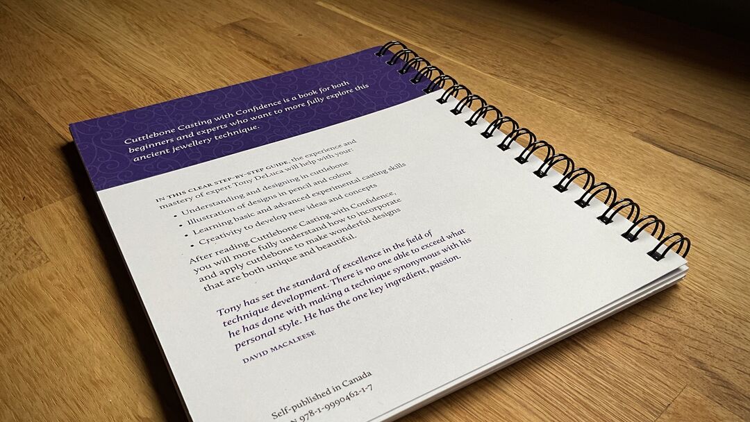 The back cover of "Cuttlebone Casting with Confidence" notebook with text and a purple cover lies open on top of a wooden table.