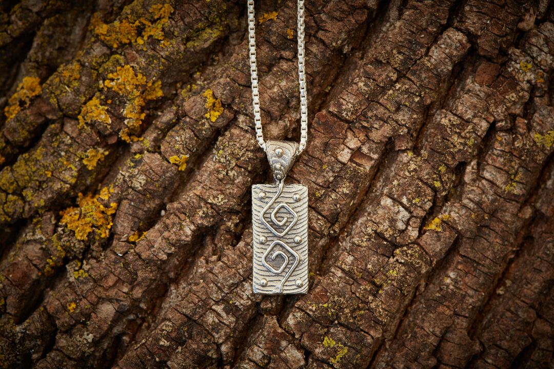 Cuttlebone cast rectangular pendant and necklace in gold set against the bark of a tree.