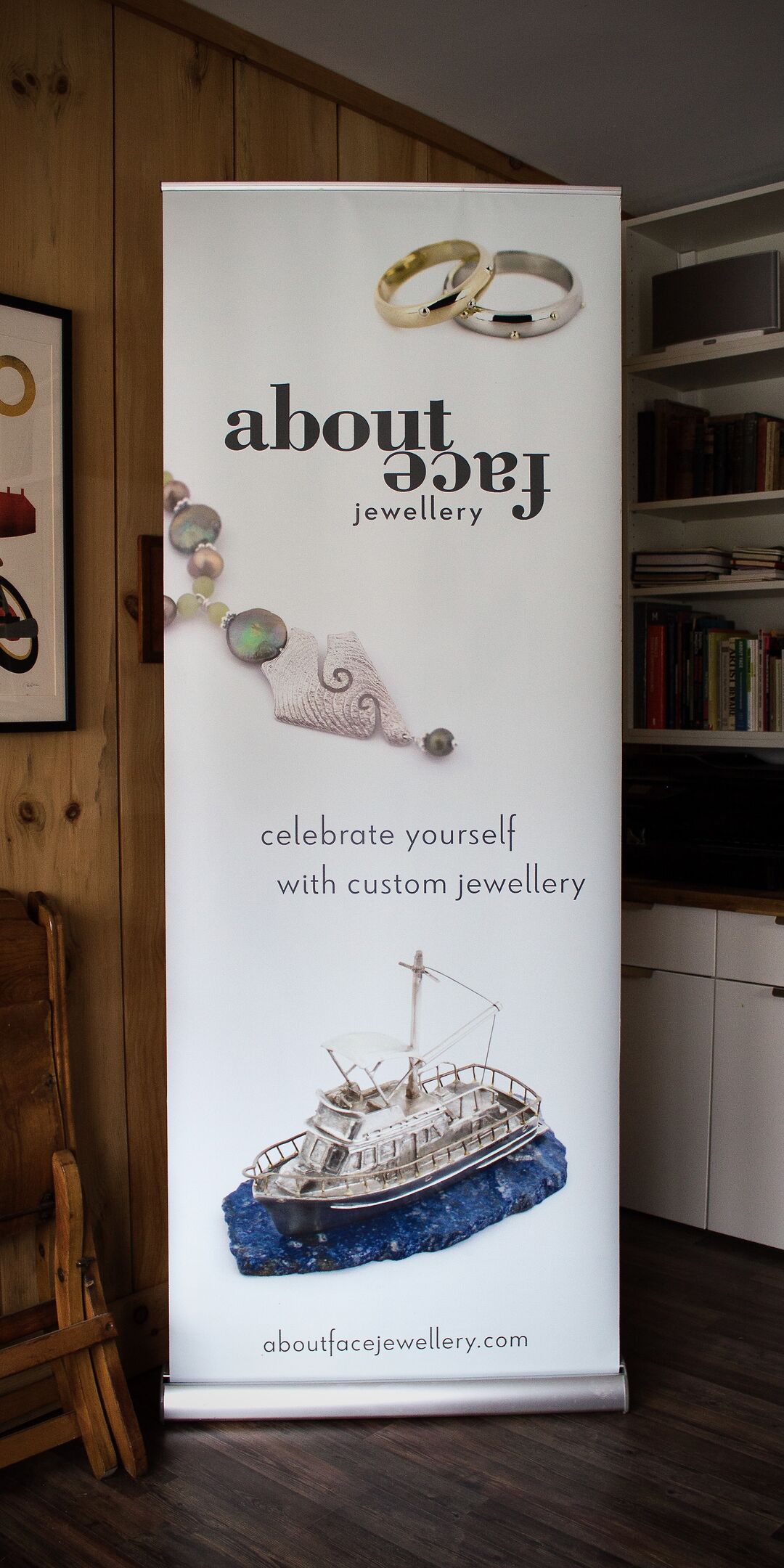 Aboutface Jewellery 2.5x6' trade show display stand featuring two rings, a necklace, and silver boat reliquary on white background